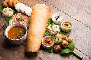 Group of South Indian food like Masala Dosa, Uttapam, Idli/idly, Wada/vada, sambar, appam, semolina halwa, upma served over banana leaf with colourful chutneys, selective focus