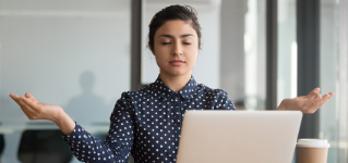 Calm office worker hindu woman sit at desk near laptop folded fingers mudra gesture take break resting at workplace do yoga exercise practise breath technique reduce stress, no anxiety at work concept