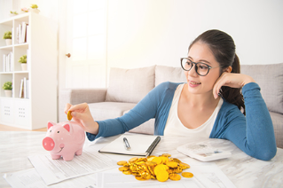 young mixed race asian woman deposit gold coin into piggy bank for future life sitting on sofa drinking coffee in the living room at home. interior and domestic housework concept.