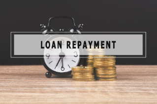 Alarm clock and gold coin stack on wooden table and black background with text LOAN REPAYMENT.