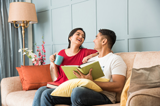 Young Indian asian couple reading books while sitting on sofa at home, modern living space