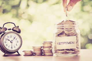 Hand putting Coins in glass jar with retro alarm clock  for time to money saving for retirement concept , vintage retro color tone