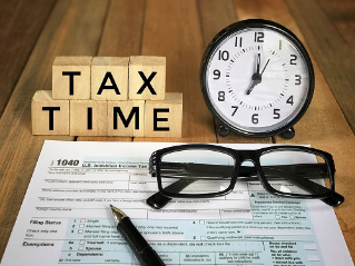 Tax-filling concept - ‘Tax time’ words on wooden blocks, pen, eyeglasses, featuring half of U.S IRS 1040 form. With vintage-styled background.