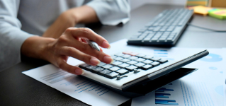 Blurred hand of Asian woman pressing calculate for prepare information of report to correct. Still holding a paper work of chart to recheck, analyze data for making presentation meeting or discussion